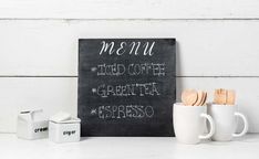 a chalkboard sign sitting on top of a table next to cups and utensils