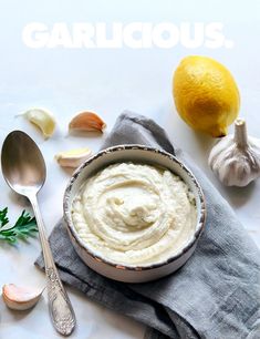 a bowl filled with white sauce next to garlic and lemon