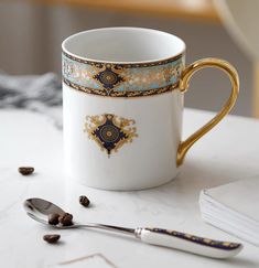 a white and gold coffee cup sitting on top of a table next to a spoon