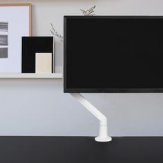 a flat screen tv sitting on top of a desk next to a vase with flowers