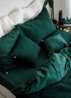 a bed with green sheets and pillows on top of it next to a plant in the corner