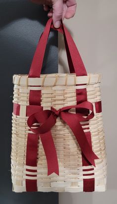 a person is holding a woven basket with red ribbon on the front and back ends