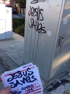 someone holding up a piece of paper with graffiti on it in front of a refrigerator