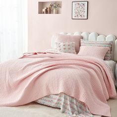 a bed with pink sheets and pillows in a room next to a white headboard