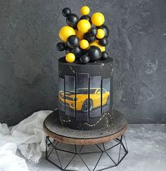 a cake with yellow and black balloons on top, sitting next to a gray wall