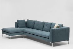 a blue sectional sofa with pillows on it's back and legs, in front of a white wall