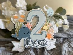 a close up of a number two sign on a bed with flowers in the background