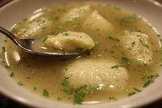 a white bowl filled with dumplings covered in broth and garnished with parsley