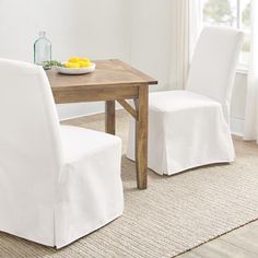 a dining room table with two white chairs and a bowl of fruit on the table