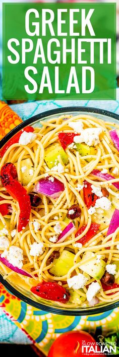 greek spaghetti salad with feta cheese and red onions in a glass bowl on a colorful cloth