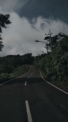 an empty road with power lines and trees on both sides under a cloudy blue sky