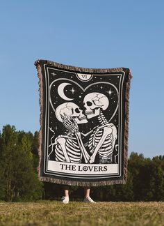 two skeletons holding up a tarp with the words the lovers on it