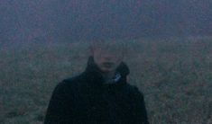 a man standing in the middle of a field on a foggy night with an umbrella