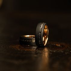 two wedding rings sitting on top of a wooden table next to each other with gold and black inlays