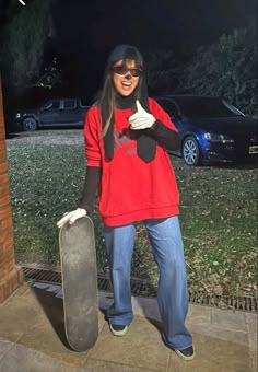 a woman standing in front of a brick building holding a skateboard and giving the thumbs up sign