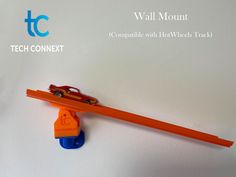 an orange and blue toy car is on top of a wall next to a pencil