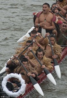 a group of men riding on top of a boat in the water with paddles