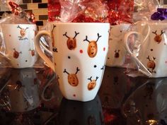 three coffee mugs with reindeer designs on them sitting on a counter next to some wrapped presents