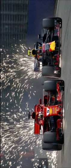 two red race cars driving down a street with fireworks in the air behind them and onlookers watching