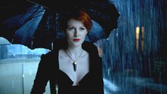 a woman with red hair and blue eyes is holding an open umbrella in the rain