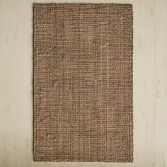 a brown rug on top of a wooden floor next to a white wall with a plant in the corner