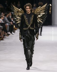 a man with wings on the runway at paris fashion week, in black and gold