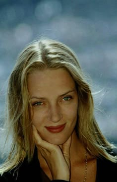 a woman with long blonde hair and blue eyes posing for a photo in front of the ocean