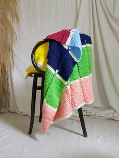 a multicolored crocheted blanket sitting on top of a chair next to a plant