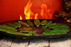 green leafy food being cooked on an iron skillet with flames in the background