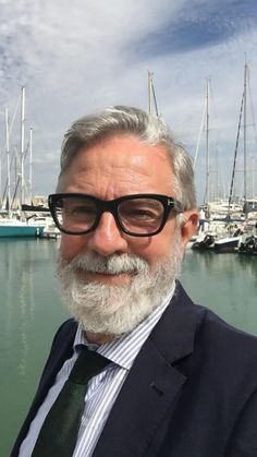 a man wearing glasses and a suit standing in front of some water with sailboats