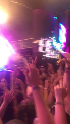 a crowd of people at a concert with their hands in the air and lights on