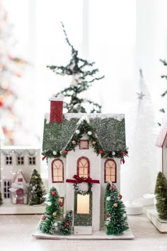 a small white house with christmas decorations on the roof and trees in front of it