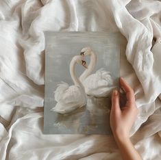 a painting of two swans in water being held by someone's hand on a bed