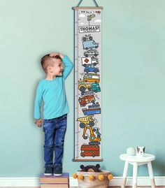 a young boy standing in front of a growth chart with cars and trucks on it