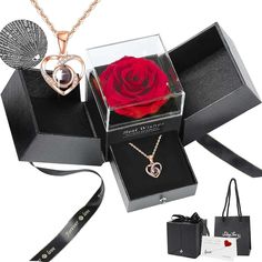 a rose in a gift box with two necklaces and a heart shaped pendant on it