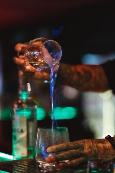 a person pouring something into a glass on top of a table with bottles and glasses