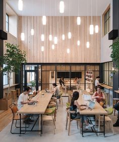 people are sitting at tables in an open area with wood paneling and hanging lights