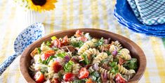 a wooden bowl filled with pasta salad next to a blue and white checkered table cloth