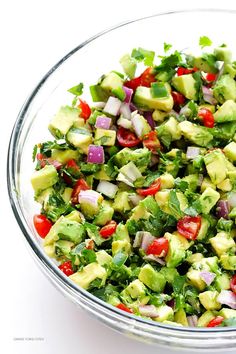 a salad in a glass bowl with avocado, tomatoes and cilantro