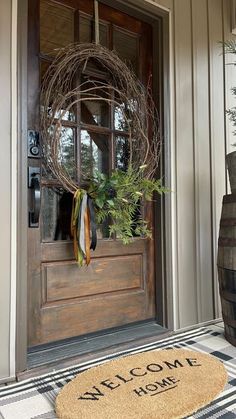 a welcome mat on the front door of a house with a wreath and potted plant