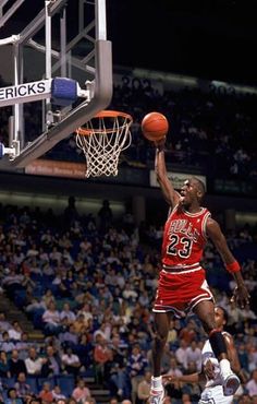 a basketball player dunks the ball in front of his opponent during a game with fans watching