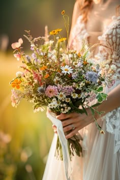 a woman holding a bouquet of wildflowers and daisies in her hands, outdoors