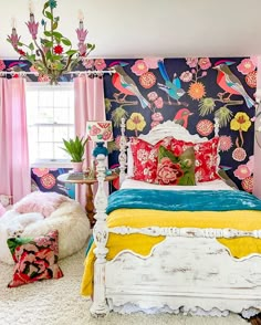 a bedroom decorated in pink, blue, and yellow with flowers on the wall behind the bed