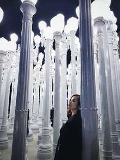 a woman standing between two tall white poles with lights on them in the middle of a room