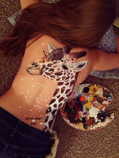 a woman with her body painted like a giraffe and painting palettes on her stomach