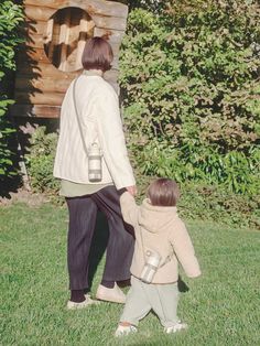 a woman holding the hand of a small child in front of a wooden structure with trees