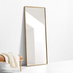 a mirror sitting on top of a wooden bench next to a white wall and chair