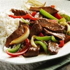 a white plate topped with beef and peppers next to rice on top of a table