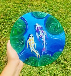 a hand holding a frisbee with two goldfishs on it in the grass