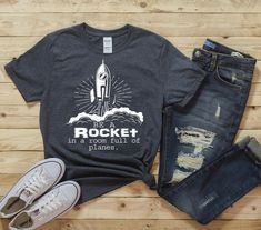 This unisex basic softstyle T-Shirt, featuring Be a ROCKET in a room full of planes, makes for a great staple t-shirt that compliments any outfit. It's made of a heavier cotton and the double-stitched neckline and sleeves give it more durability, so it can become an everyday favorite. NOTE: Sleeves are rolled up in the ad photo.  OPTION TO CHANGE ROCKET SHIP COLOR *100% ring-spun cotton* *Fabric weight: 4.5 oz/y² (153 g/m²) *Pre-shrunk for extra durability *Shoulder-to-shoulder taping *Quarter-t Space Theme Teacher Shirt, Team Shirt Designs, Space Tshirt, Nasa Shirt, Camper Shirt, Teach Love Inspire, Space Shirts, Space Center, Rocket Ship